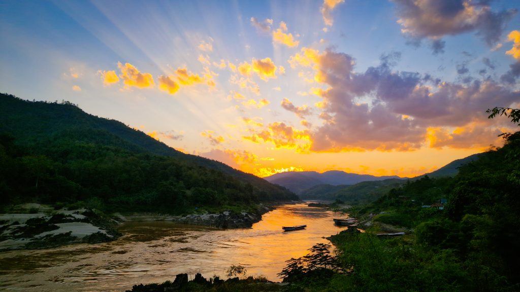Sonnenuntergang über den Bergen und dem Fluss Mekong mitten in der grünen Natur in Laos. Die Sonne erstrahlt die Wolken in feurigem Gelb.