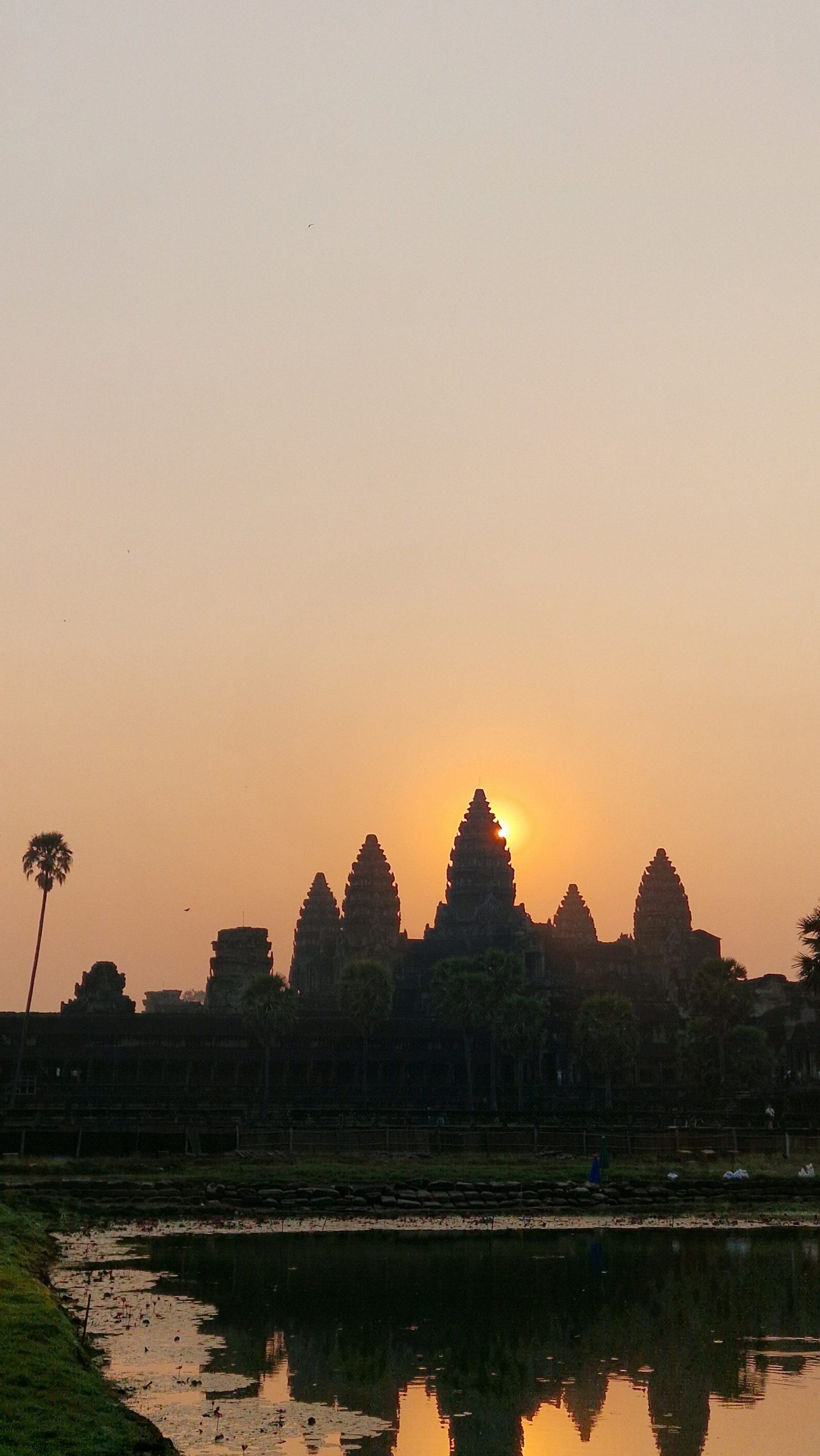 Sonnenaufgang bei Angkor Wat. Die Sonne scheint orange hinter dem mittleren Turm hervor.