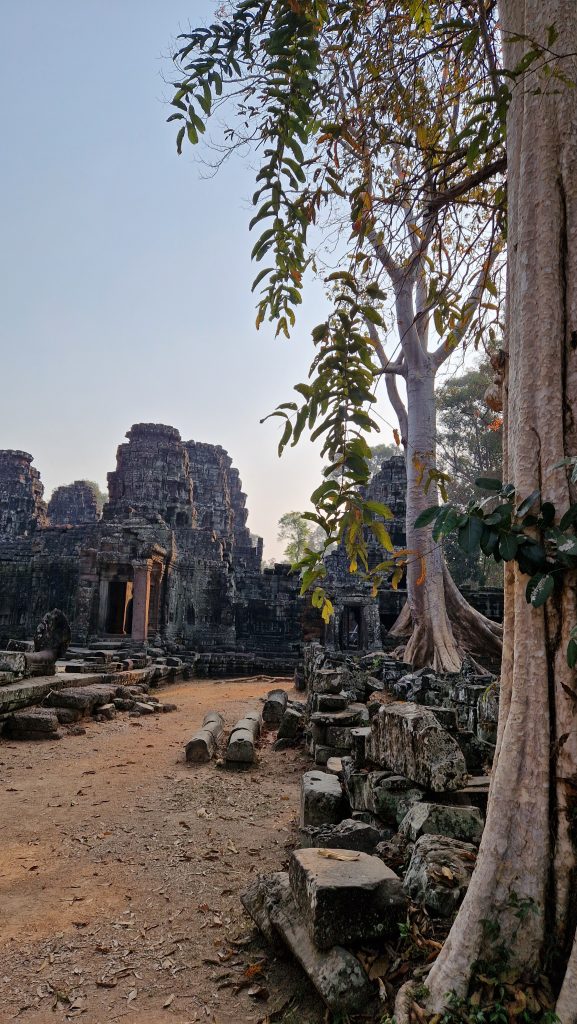 Außenansicht des Bayon Tempels. Steintürme ragen in den Himmel. Davor liegen vereinzelte Steine.