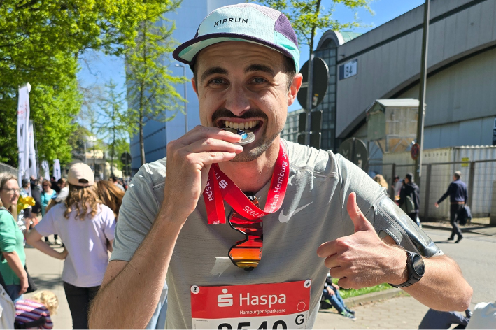 Philippe grinst und beißt auf seine Medaille nach dem Schaffen des Hamburg Marathons