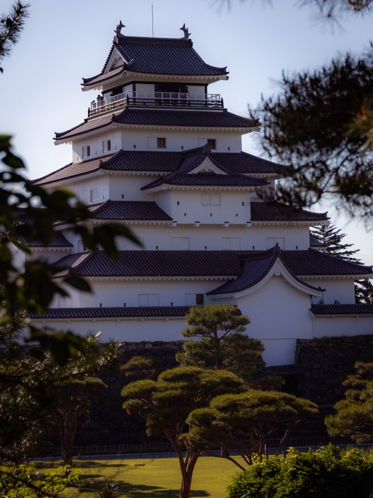 Burg Tsuruga in Aizu Wakamatsu mit vielen Dächerebenen umgeben von einem grünen Park.