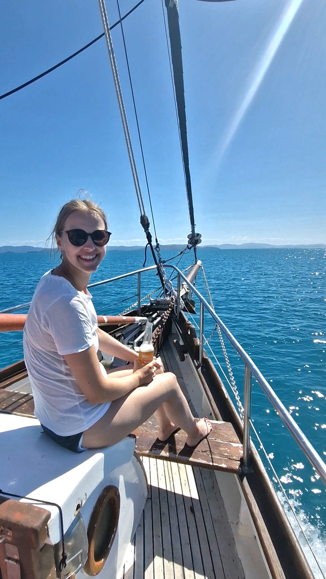 Lena sitzt mit Bier am Bug des Segelboots und lächelt