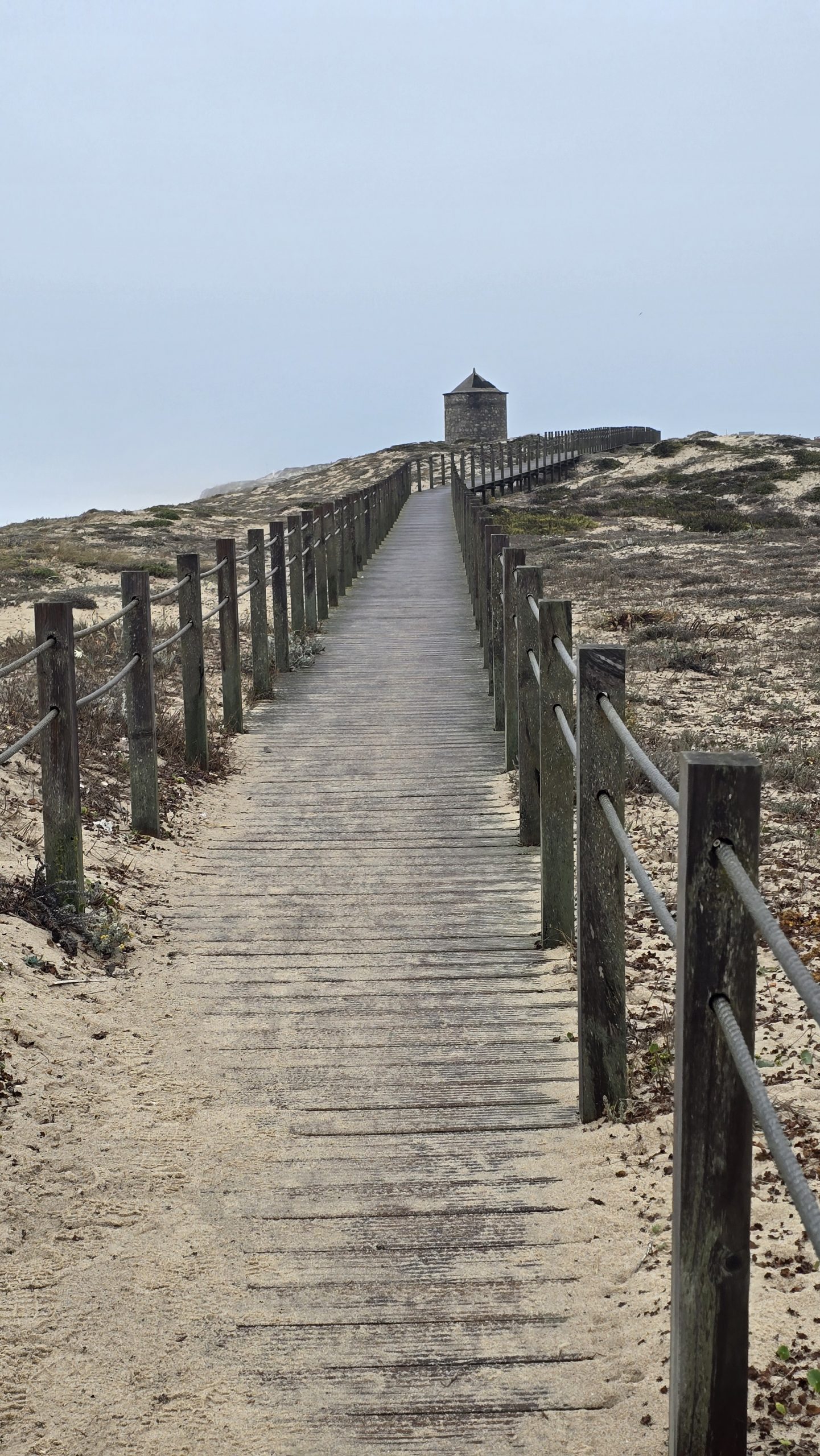 Ein Holzpfad führt durch die Sanddünen hinauf zu einem kleinen Steinhaus