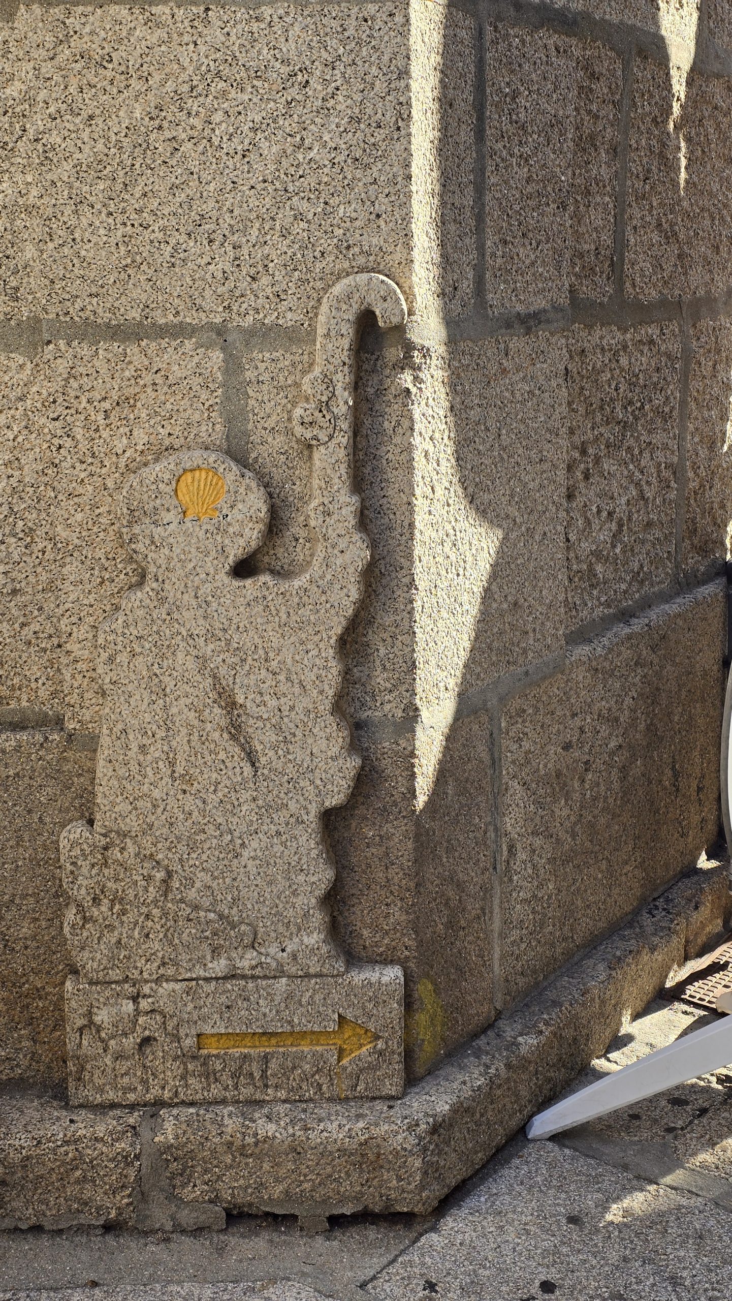 Eine Steinfigur in der Form eines Bischofs mit einer gelben Jakobsmuschel auf dem Hut