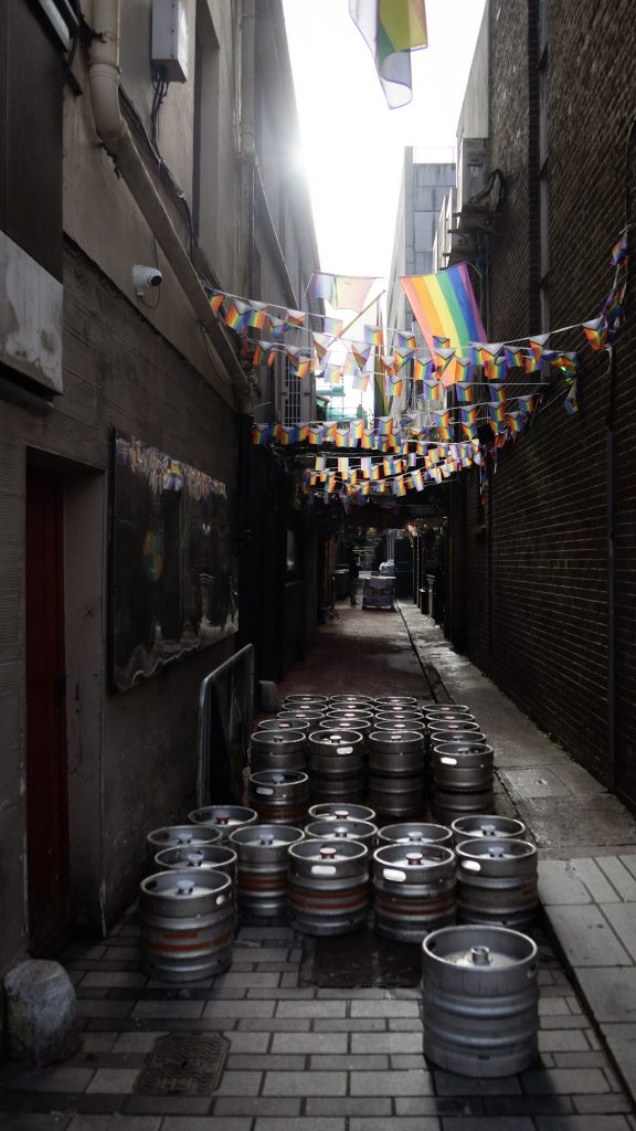 Blick auf eine Gasse in Cork mit Bierfässern und Pride Fahnen