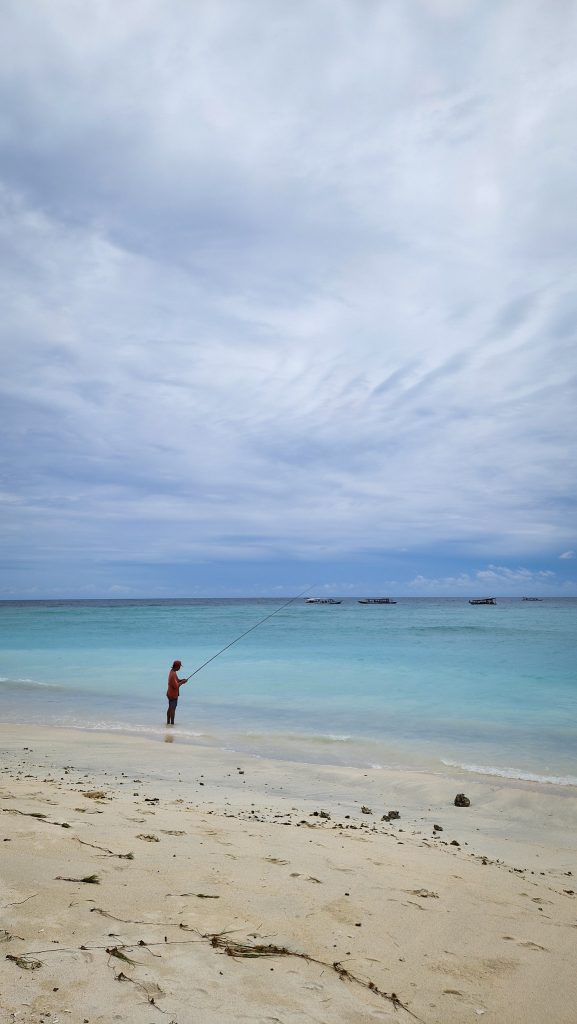 ein Angler am Strand von Gili Meno mit türkisblauem Wasser