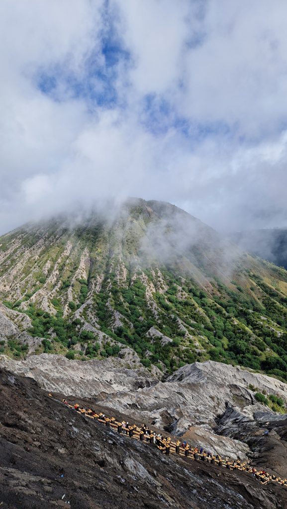 Blick auf das graue mit grünen Pflanzen bewachsene Gestein eines Vulkans