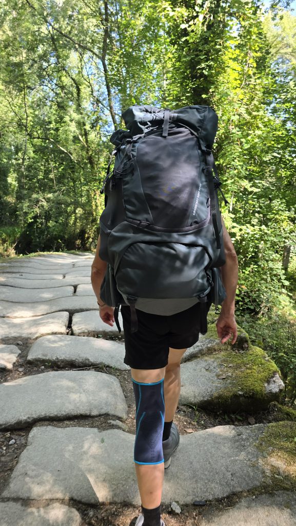 Wandern über eine alte Steinbrücke in grünen Wald mit einer Person mit Wanderucksack von hinten