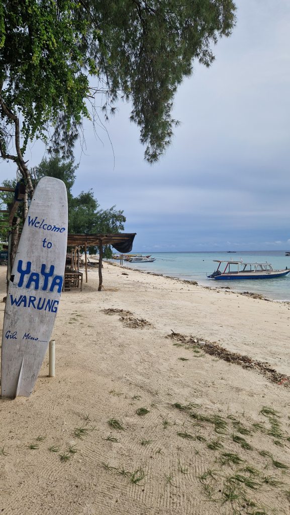 Strand von Gili Meno mit einem lokalem Restaurant (Warung) und einem Holzboot im Wasser