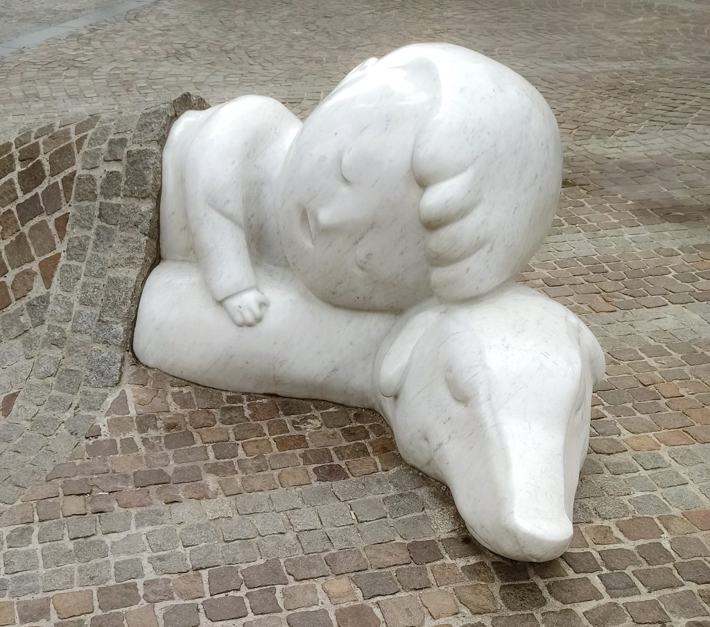 Eine Nahaufnahme der weißen Figuren Nello und Patrasche eingebettet im Kopfsteinpflaster