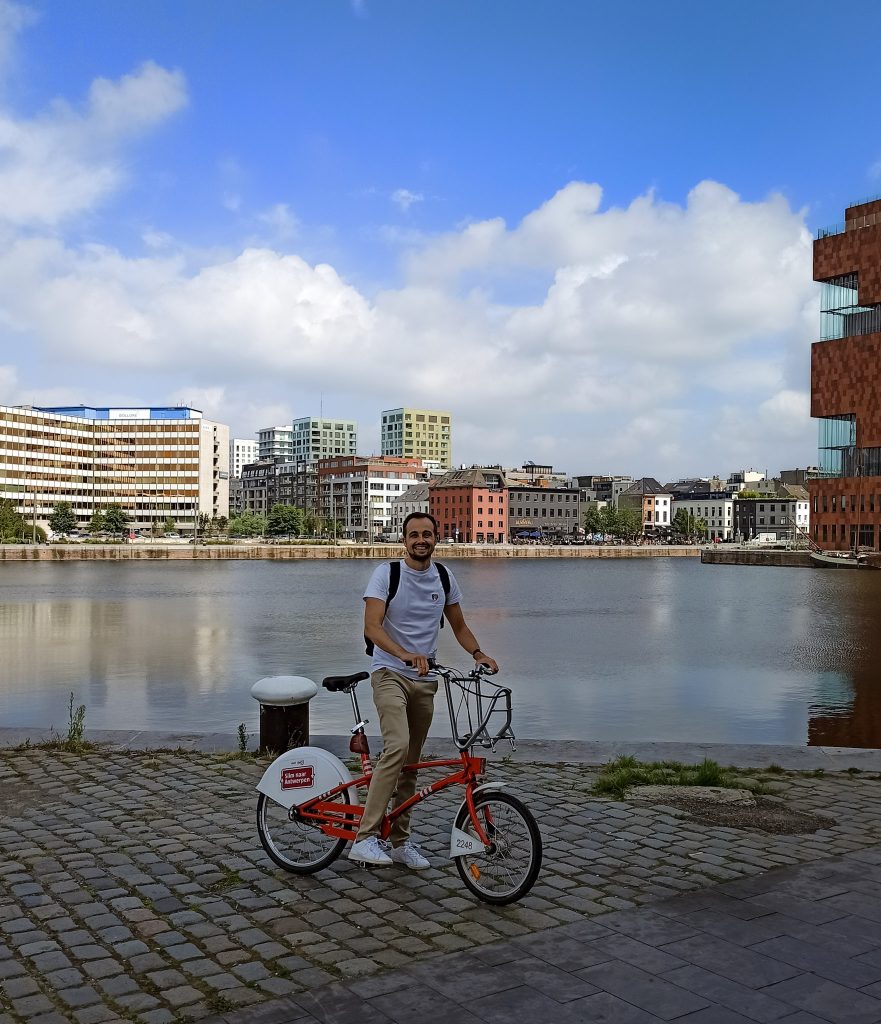 Eine Person mit einem der geliehenen Velo City Bikes von Antwerpen vorm Hafenbecken