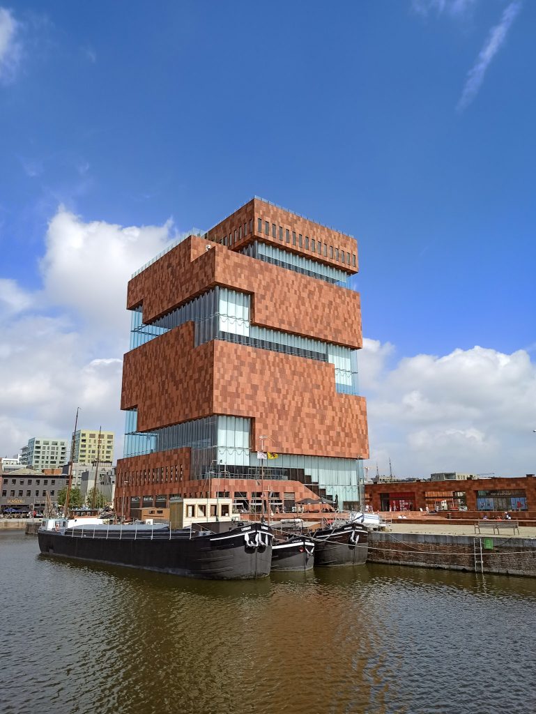 das MAS Museum bestehend aus Backstein und Glas. Davor befindet sich das Hafenbecken mit zwei größeren Schiffen.