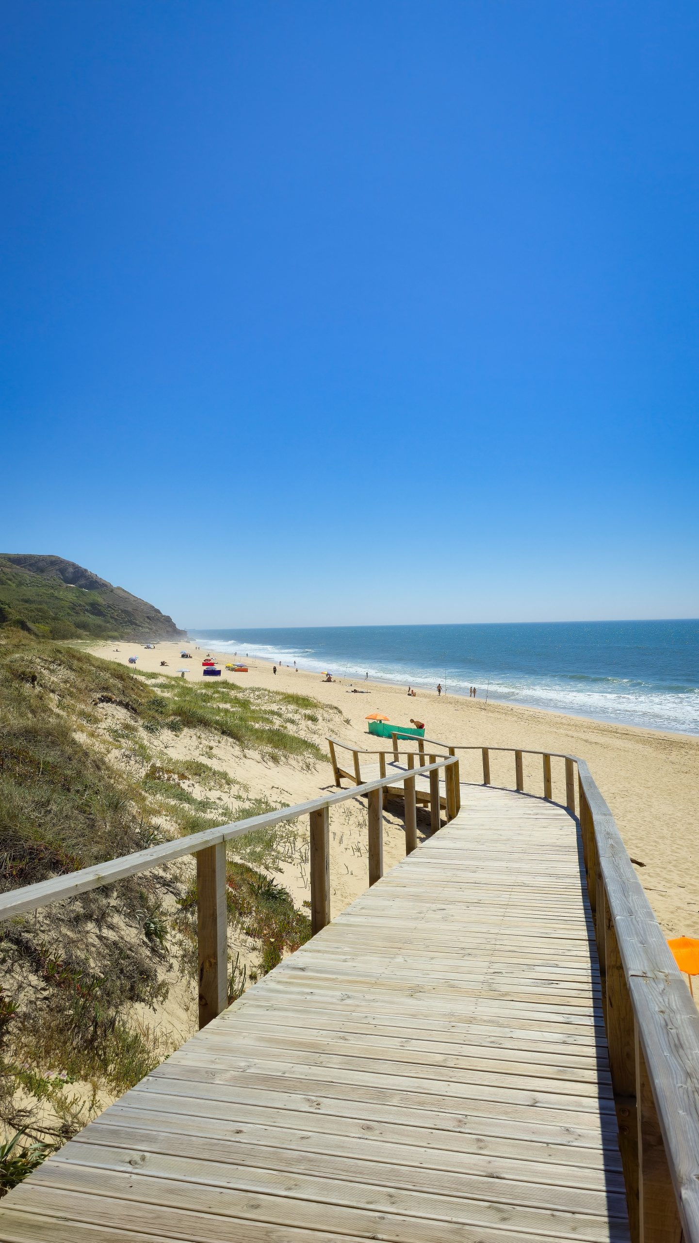Portugals Westküste: Kilometerlanger Sandstrand von Murtinheira. Menschenleer mit einem Holzweg über die Dünen, strahlend blauer Himmel und der Atlantik.