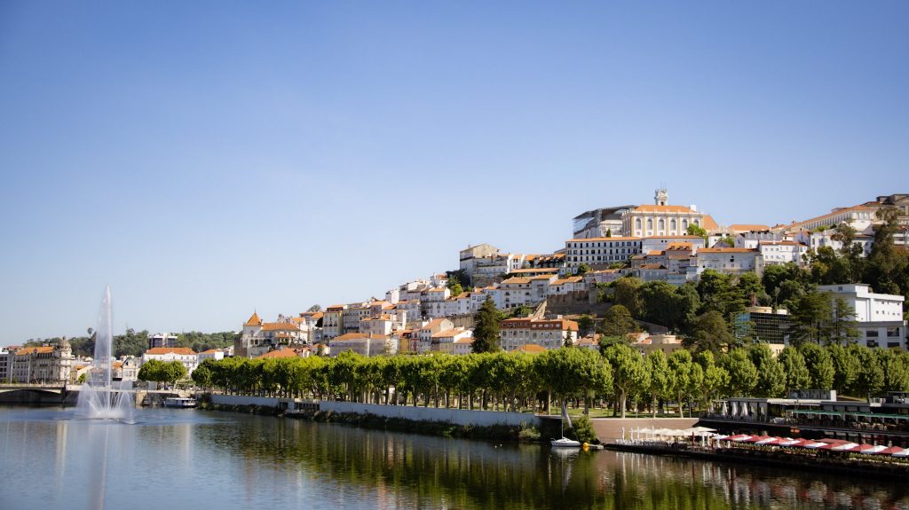 Blick auf die Universitätsstadt Coimbra, die auf einem Hügel gelegen ist. Davor der Fluss Mondego.