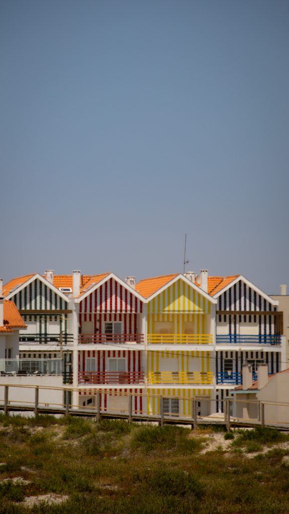 bunt-weiß-gestreifte Häuser, ehemalige Fischerhütten, vor den Dünen in den Ort Costa Nova